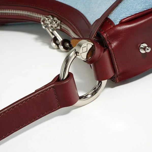 Close-up of a burgundy leather and denim handbag with silver hardware ring detail
