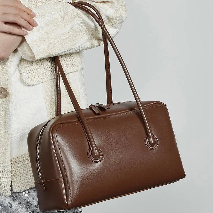 Woman holding brown leather handbag with long handles and zip closure