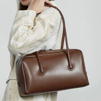 Woman in cream jacket carrying a brown leather handbag on shoulder