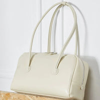 Cream leather handbag with double handles on a light background