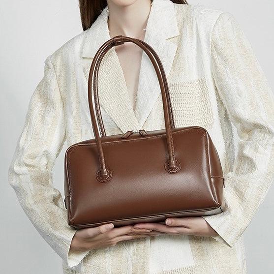 Woman holding a brown leather handbag in a textured cream blazer