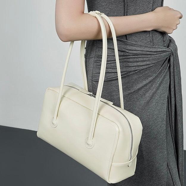 Woman in grey dress holding cream leather shoulder bag