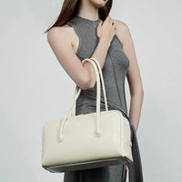 Woman in gray dress holding a white leather handbag with double handles