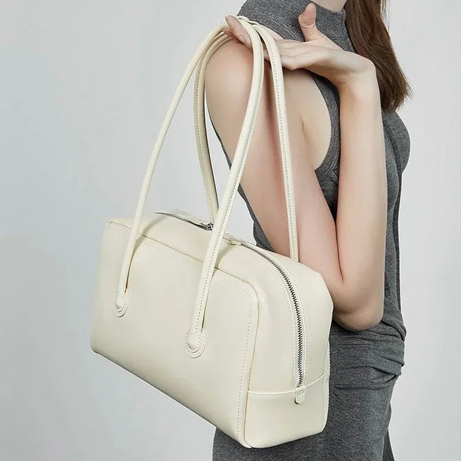 Woman in grey dress holding a cream leather handbag with double shoulder straps