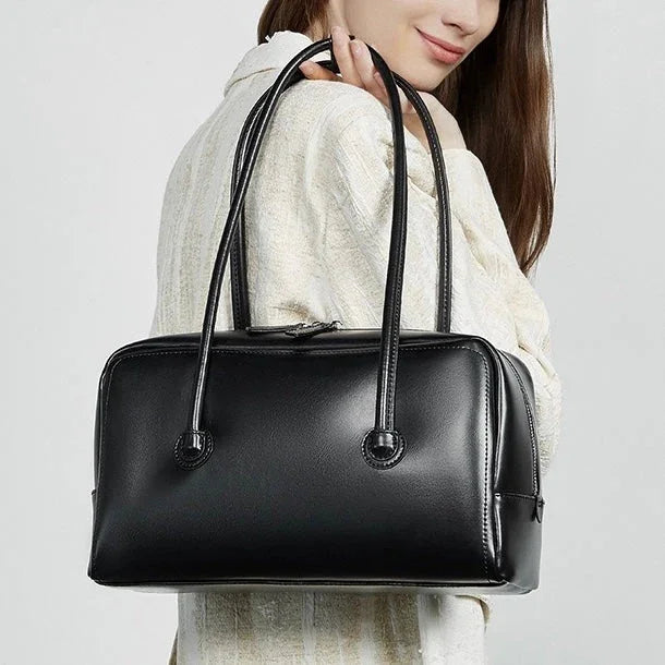 Woman holding a black leather handbag with double straps, minimal design, fashion accessory