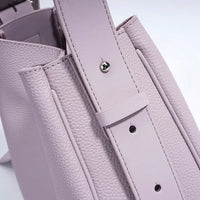 Close-up of a light purple textured leather handbag with adjustable strap and silver hardware