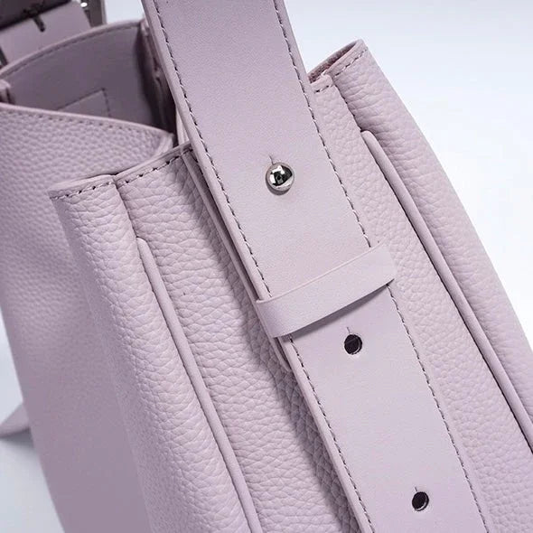 Close-up of a light purple textured leather handbag with adjustable strap and silver hardware