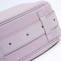 Closeup of a light purple leather bag with textured surface and belt strap detail