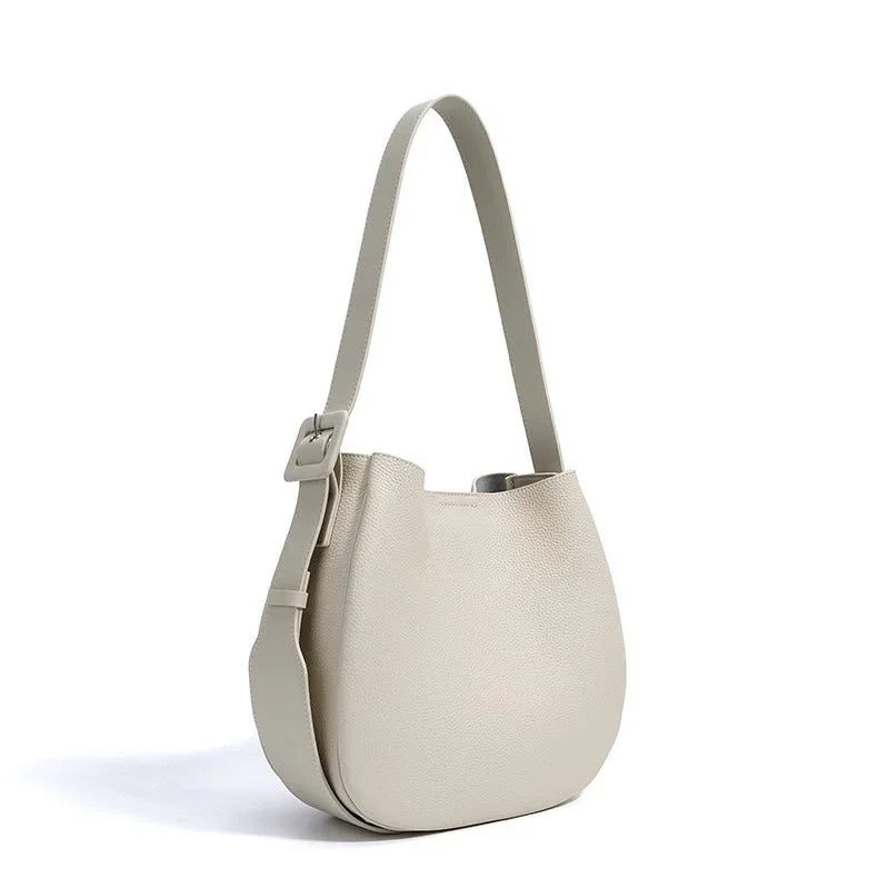 Beige leather bucket bag with wide adjustable shoulder strap on white background