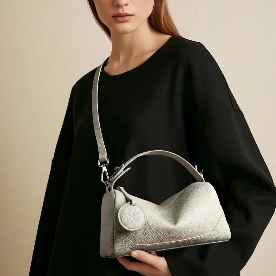 Woman in black top holding a minimalist light gray leather handbag with handle and strap