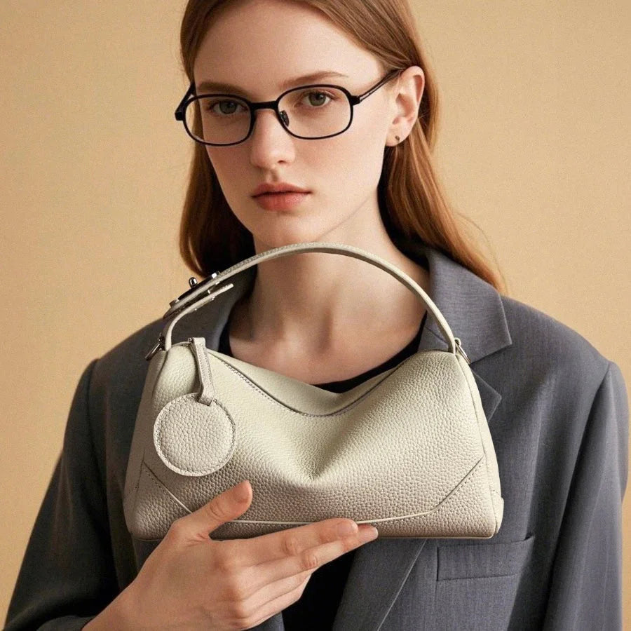 Woman in glasses and grey blazer holding textured cream leather shoulder bag