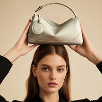 Woman in black suit holding a textured white leather handbag above her head, beige background