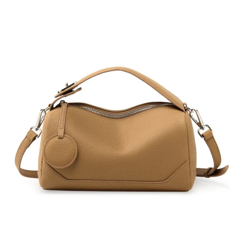Tan leather handbag with top handle, detachable strap, and zip closure on white background.