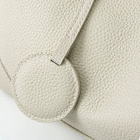 Close-up of textured beige leather handbag with round accent and visible stitching
