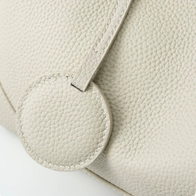 Close-up of textured beige leather handbag with round accent and visible stitching