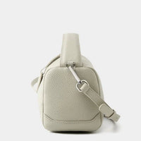 Side view of a light beige pebbled leather crossbody bag with adjustable strap