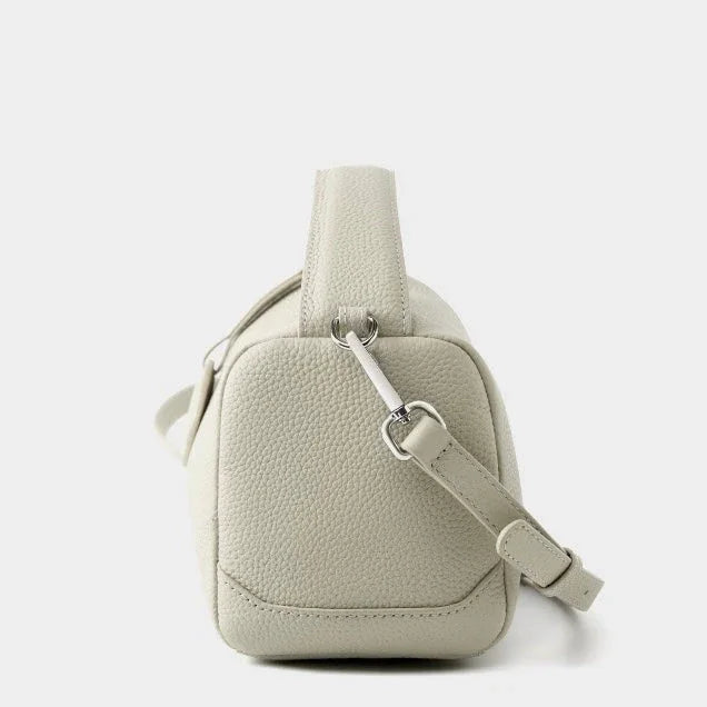 Side view of a light beige pebbled leather crossbody bag with adjustable strap