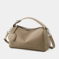 Taupe leather handbag with top handle, detachable strap, and zipper closure on white background