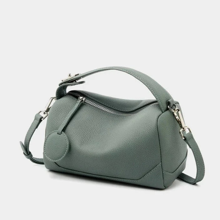 Sage green leather handbag with zipper, short handle, and shoulder strap on white background