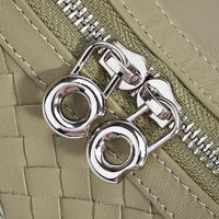Close-up of silver zipper pulls on a woven sage green leather bag