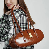 Woman holding oval brown leather handbag with gold clasp, wearing plaid jacket