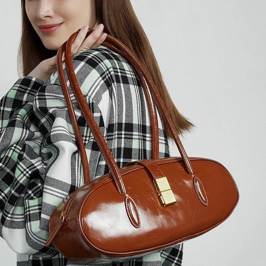 Woman holding oval brown leather handbag with gold clasp, wearing plaid jacket