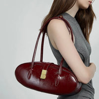Woman wearing chic red leather shoulder bag with gold clasp, gray sleeveless top, neutral background