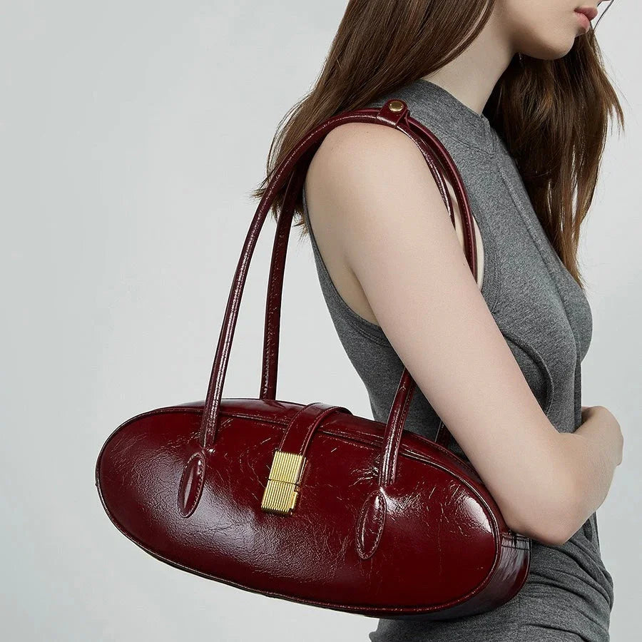 Woman wearing chic red leather shoulder bag with gold clasp, gray sleeveless top, neutral background