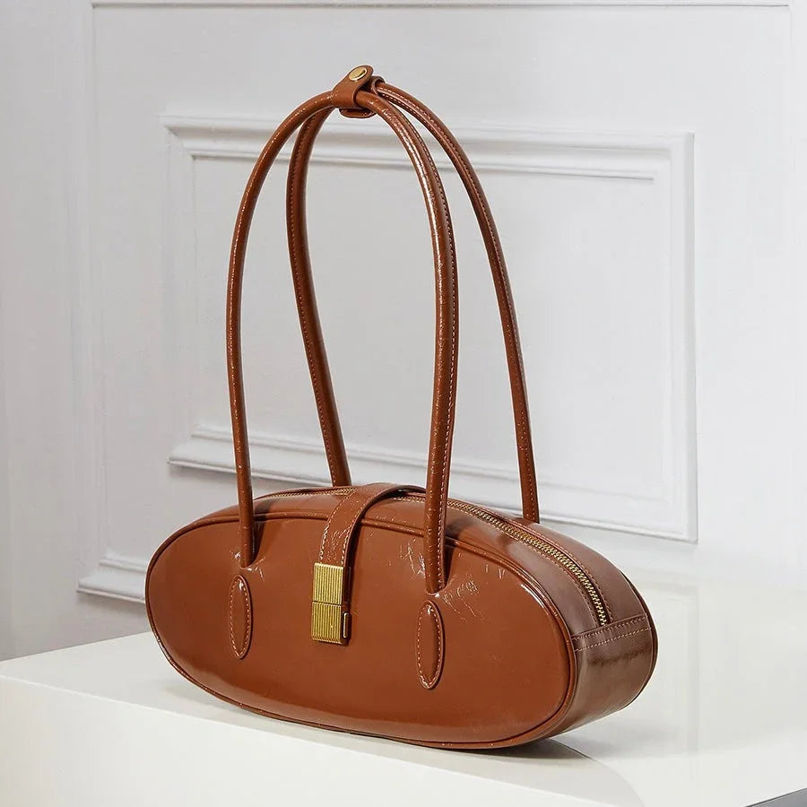 Brown oval leather handbag with long handles and gold clasp on white background