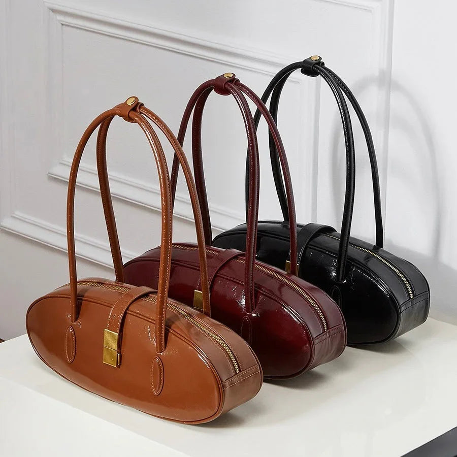 Three oval leather handbags in brown, burgundy, and black on a white table