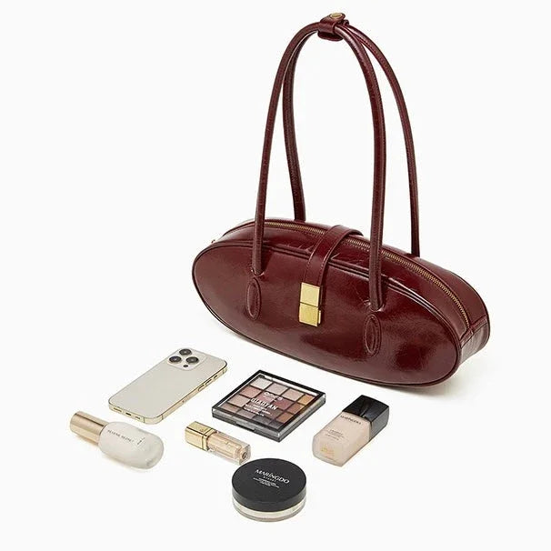 Burgundy oval leather handbag with makeup, perfume, phone and cosmetics on white background