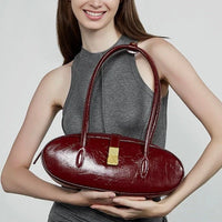 Woman holding a glossy burgundy oval handbag with gold clasp, grey sleeveless dress