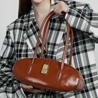 Woman in plaid blazer holding oval brown leather handbag with gold clasp
