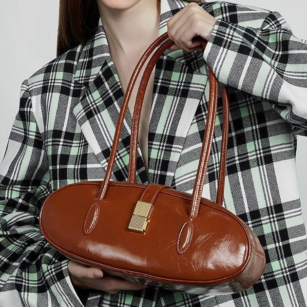 Woman in plaid blazer holding oval brown leather handbag with gold clasp