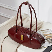 Glossy burgundy leather handbag with double handles on cream fabric, modern setting