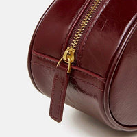 Close-up of burgundy leather round handbag with gold zipper on white background