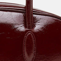 Close-up of glossy dark red leather handbag handle and stitching detail
