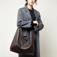 Woman in gray coat holding large brown leather tote bag