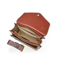 Brown leather handbag with open flap, spacious interior, zipper pocket, and colorful strap