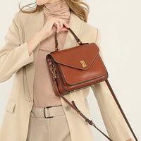 Woman in beige suit holding brown leather crossbody handbag