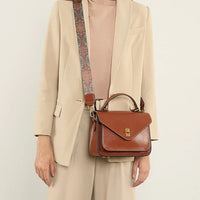 Woman in beige suit carrying brown leather crossbody satchel with patterned strap