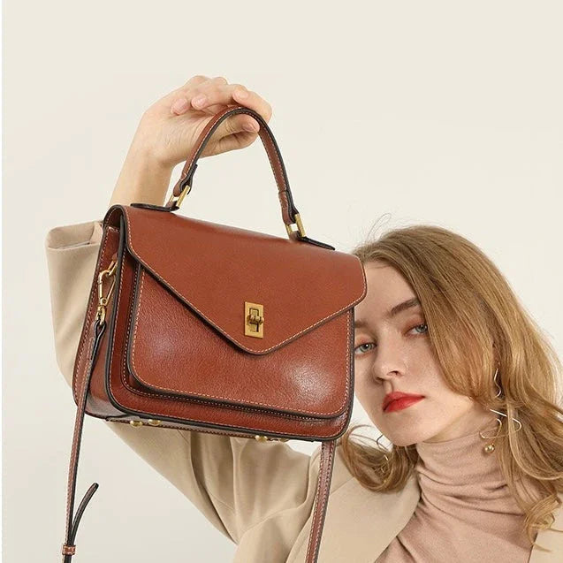 Woman holding elegant brown leather handbag with gold clasp and top handle
