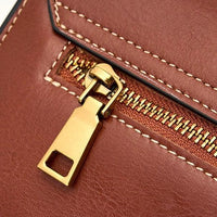 Close-up of a gold zipper on a brown leather bag with white stitching detail