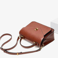 Brown leather crossbody bag with gold buckle and straps on a white background