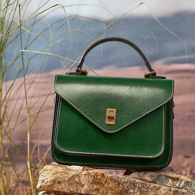 Green leather handbag with top handle on rocks outdoors, nature background
