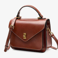 Brown leather crossbody satchel bag with gold hardware and top handle on white background