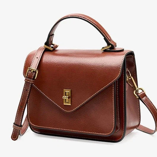 Brown leather crossbody satchel bag with gold hardware and top handle on white background