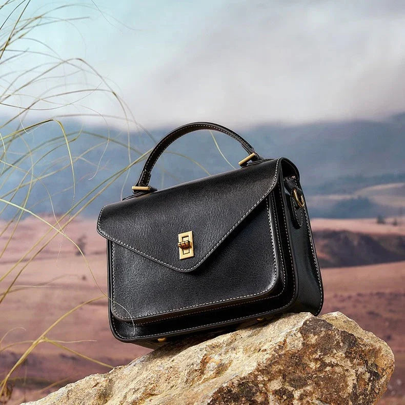 Black leather handbag with gold clasp on rock in outdoor landscape with hills