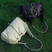 Black and white quilted handbags with chain straps on green grass