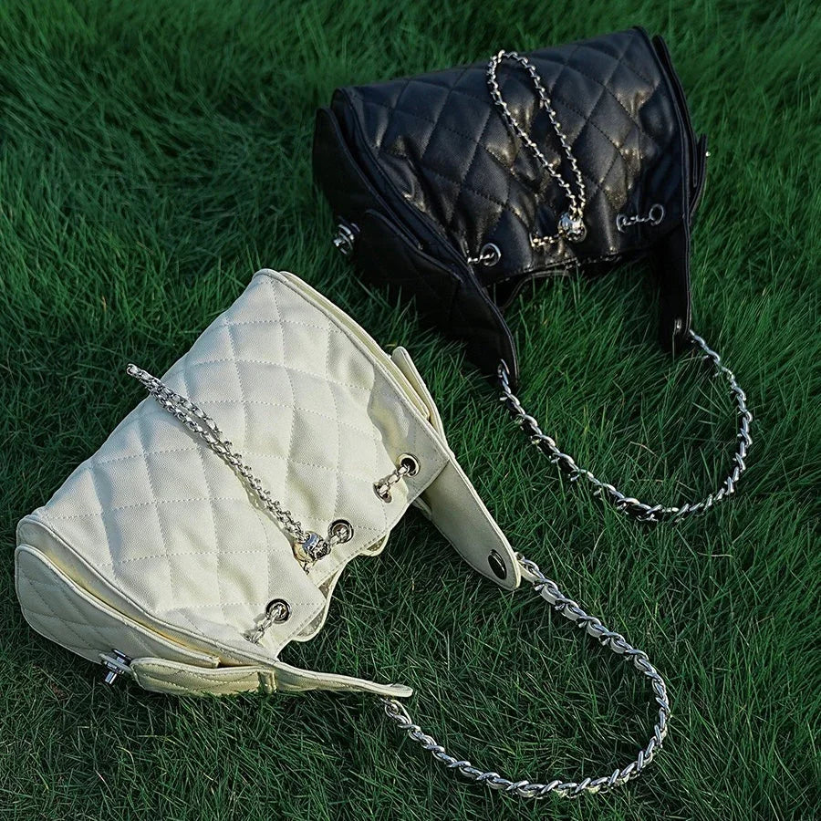 Black and white quilted handbags with chain straps on green grass